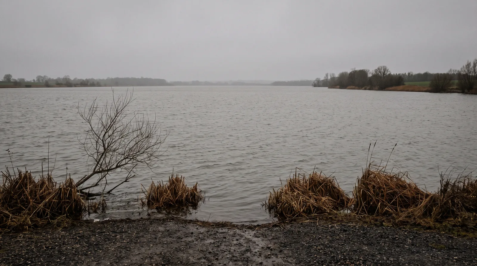 Un grand lac à midi sous un plafond gris parfaitement uniforme, sans ligne d'horizon nette entre le ciel et l'eau